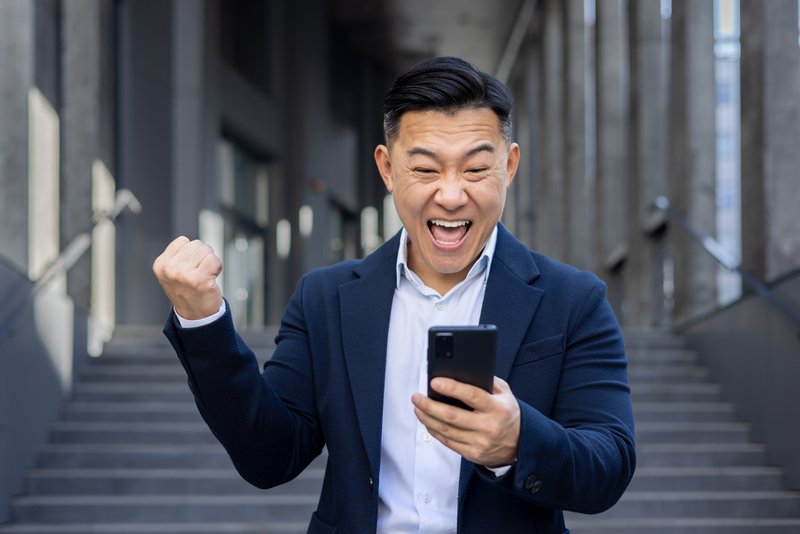 Euphoric business professional enjoys a moment of success with clenched fist up, joyously using smartphone